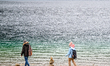 Two hikers wearing winter clothing and backpacks walk along the pebble shoreline of Lake E...