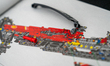 LEGO Technic Ferrari SF-24 body parts and a red connector piece are shown atop the printed...