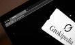 The Grokipedia website appears on a laptop computer screen, and the Grokipedia logo appear...