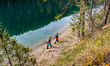 Two hikers wearing backpacks walk along the rocky shore of the clear, emerald-green Lake B...