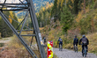 A cycling group rides mountain bikes on a gravel path next to a large electricity pylon at...