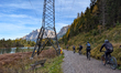 A cycling group rides mountain bikes on a gravel path next to a large electricity pylon at...