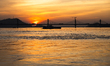 A boat sails on the river Brahmaputra during sunset, with the silhouette of a cable-stayed...