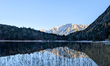 The Wetterstein Mountains and surrounding pine forest reflect on the calm water of Lake Fe...
