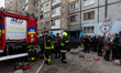 Locals stand near rescuers outside an apartment block in the Darnytskyi district damaged b...