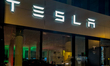 An illuminated facade of a TESLA sales showroom features large windows displaying current...