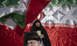 A veiled woman holds a national flag and a portrait of Iran's Supreme Leader, Ayatollah Al...