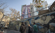 An Iranian man smiles while walking with his friends under an anti-U.S. and Israeli billbo...