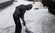 A man clears a driveway in front of his house as the temperatures dropped and snow fell in...