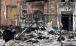 Men stand outside the entrance of a multi-storey residential building damaged as a result...