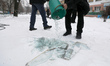 A man throws glass shards from a bucket onto the snow during a response effort to Russia's...