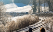 A couple sits on a wooden bench and watches a Bayerische Regiobahn (BRB) train travel thro...