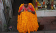 A laborer carries garlands of marigold flowers to supply at a wholesale flower market to b...