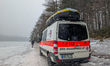 Water rescue paramedics in red protective gear stand with a vehicle on the shore of the fr...