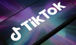 The TikTok logo appears on the screen of a smartphone placed on a reflective surface onto...