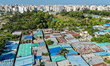 An aerial view shows a dense neighborhood of tin-roofed homes bordered by greenery, standi...