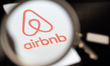 The Airbnb logo is seen through a magnifying glass on a mobile phone screen next to a key...
