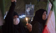 An Iranian woman holds a candle while standing under a portrait of Iran's Supreme Leader,...