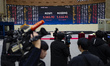 Journalists and television camera crews film the closing market figures displayed on a lar...