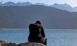 A man sits alone on the rocky shoreline of Lake Walchensee in Urfeld, Bavaria, Germany, on...