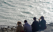 People sit on the rocky shoreline of Lake Walchensee in Urfeld, Bavaria, Germany, on March...