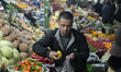 An Iranian salesperson loads a plastic bag with vegetables for a customer in a traditional...
