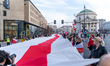 People hold a large Belarusian flag while attending a march on Freedom Day in Warsaw, Pola...