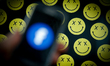 A smartphone with an out of focus Facebook logo is seen with the smiley emoticons in the b...