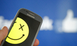 A smartphone with a smiley symbol is seen with the Facebook logo in the background in this...