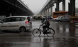 A man rides a bike as he crosses a road during rainfall on July 27, 2018 in New Delhi, Ind...