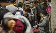 A photo showing Pedestrians looking at fur hats which an Elderly women is selling on a str...