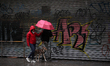 Two people and their pet walk in the rain during a massive power blackout on June 16, 201...