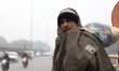 A man wrapped in warm clothes waits at a bus stop on a cold foggy morning in Gurugram on t...