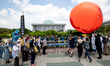Member of Climate Crisis Emergency Action activists hold a large red balloon that shapes t...