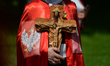 A member of the Order of Knights of Christ the King carries a wooden cross during Corpus C...