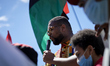 Rev. Levi Combs, III (center) speaks to the crowd after climbing on the remaining base of...