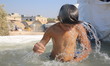 Syrian children play in a makeshift mobile swimming pool with tarpaulin at the back of a p...