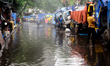 Commuters make their way along a waterlogged street following monsoon rainfalls in Dhaka,...