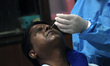 A health worker in personal protective equipment (PPE) collects a nasal swab samples from...