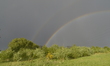 Sunlight refracting in rainwater to create a double rainbow, arching over power lines in S...
