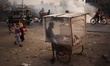 A cake vendor waits for customer inside his polythene wrapped shop as passerby make their...
