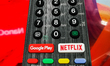 A detail of  TV remote control with streaming platform buttons is seen on the illustration...