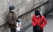 A Ukrainian woman wearing a face mask walks past a man asking for alms in Kyiv, Ukraine on...
