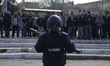 A riot police with a rubber-bullet rifle stands in front of students that chant reivindica...