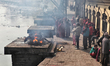 Onlookers watch as a pyre is engulfed in flame along the bank of the Bagmati River at the...