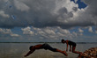 Indian boys jump to take bath in flooded River Ganges as patchy clouds loom overhead  in A...