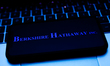 Berkshire Hathaway logo displayed on a phone screen and a laptop keyboard are seen in this...