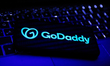 GoDaddy logo displayed on a phone screen and a laptop keyboard are seen in this illustrati...