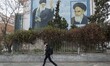 An Iranian man uses his smartphone while walking under portraits of Iran’s Supreme Leader...