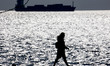 Silhouette of a woman walking with a cargo container ship in the background. Daily life in...